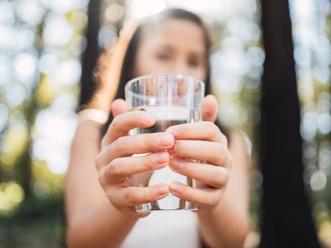 Woman holding glass of water with both hands in front of camera