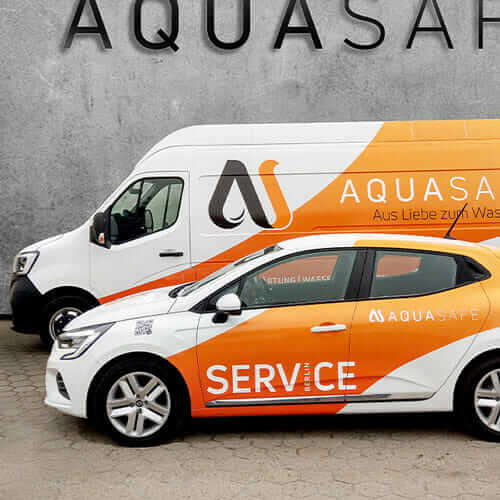 Company partner - service vehicles of the company AQUASAFE with orange vehicle livery in front of gray warehouse