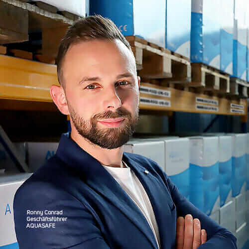 Ronny Conrad Geschäftsführer bei AQUASAFE - Im Warenlager vor Blauen Produktkartons